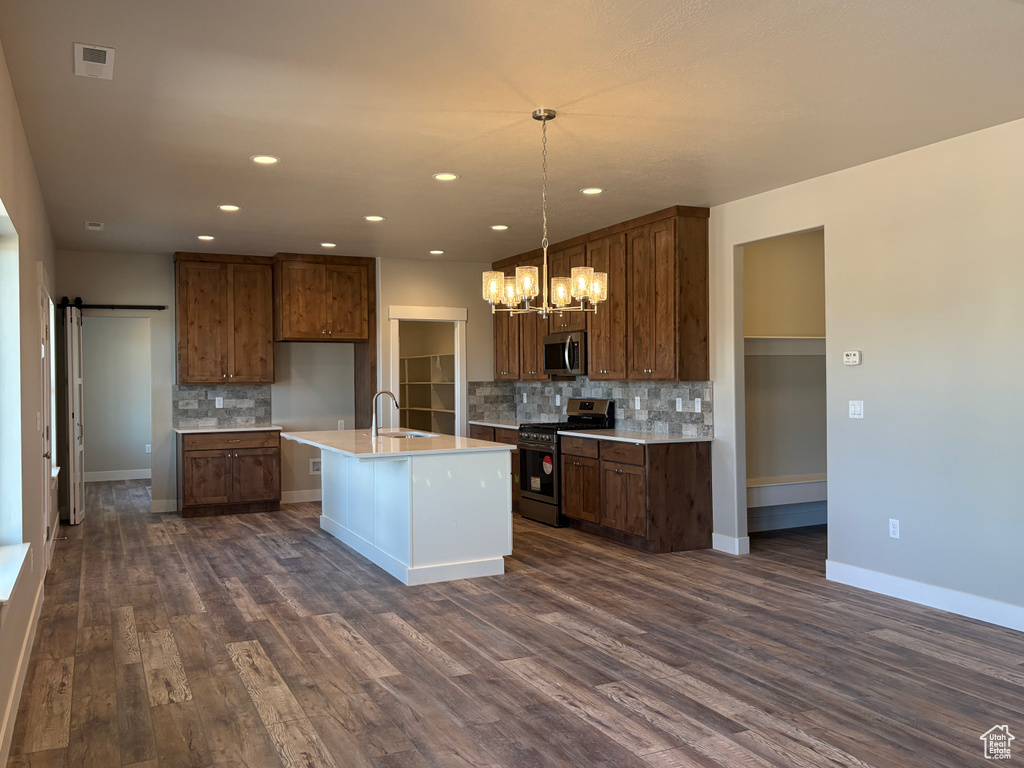 Kitchen with stainless steel appliances, a sink, backsplash, a chandelier, and dark wood-style floors
