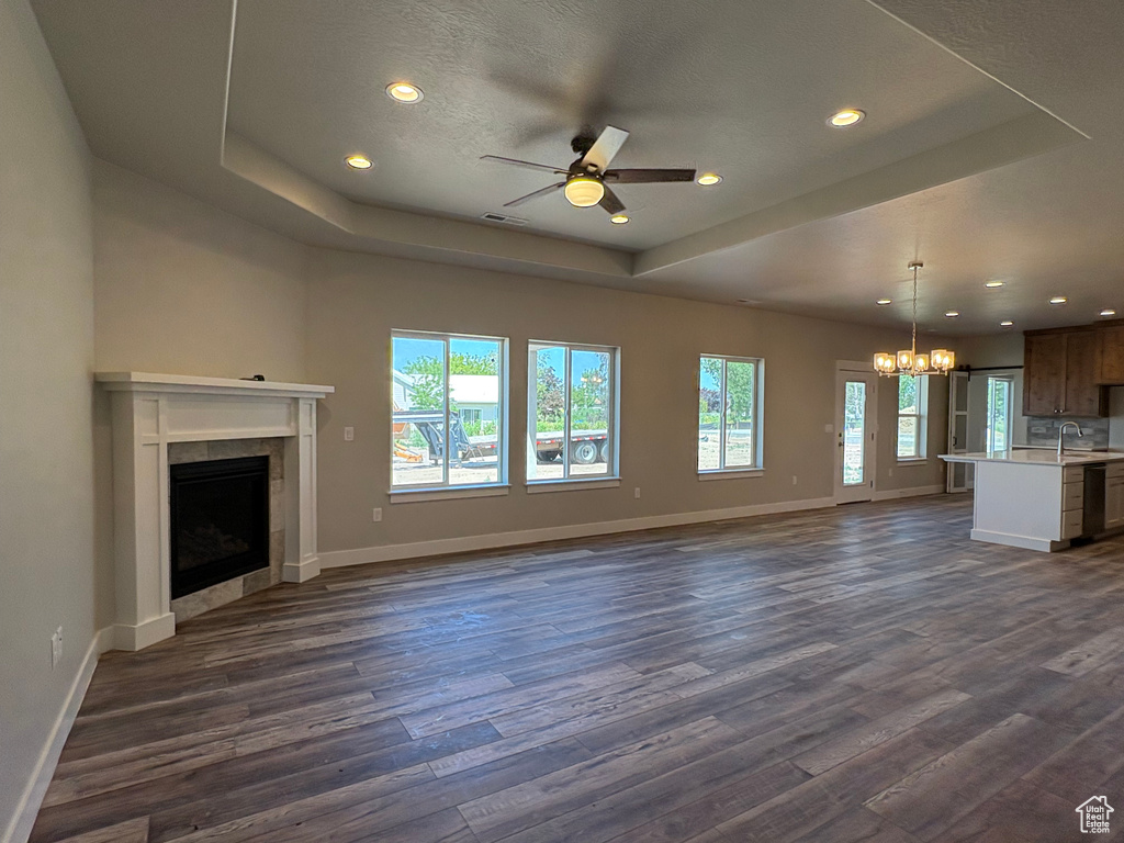 Unfurnished living room featuring a raised ceiling, a chandelier, dark wood-style flooring, a tiled fireplace, and a sink