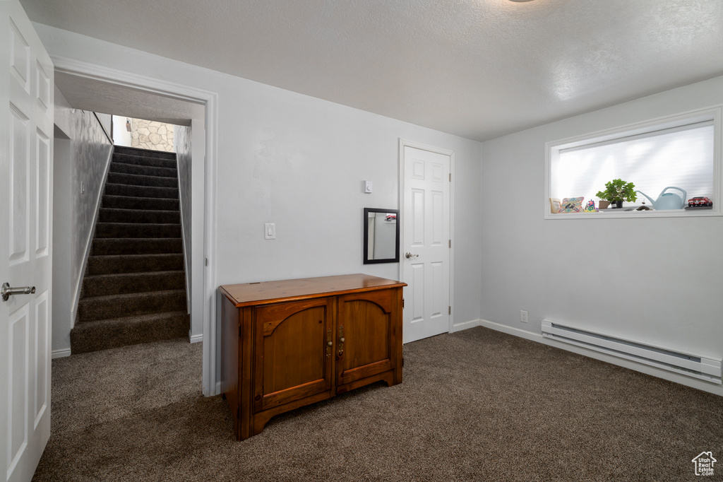 Unfurnished room featuring baseboards, stairway, dark carpet, a textured ceiling, and a baseboard radiator