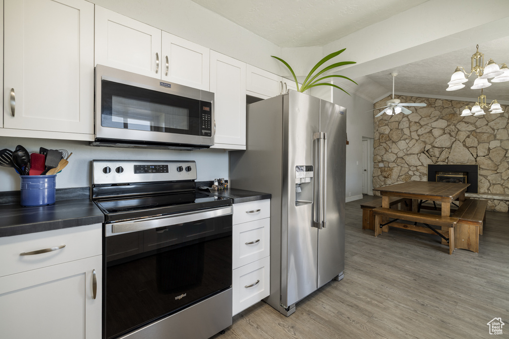 Kitchen with stainless steel appliances, lofted ceiling, dark countertops, and white cabinetry
