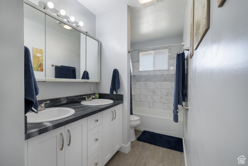 Full bath with double vanity, wood finished floors, shower / bath combo, and a sink