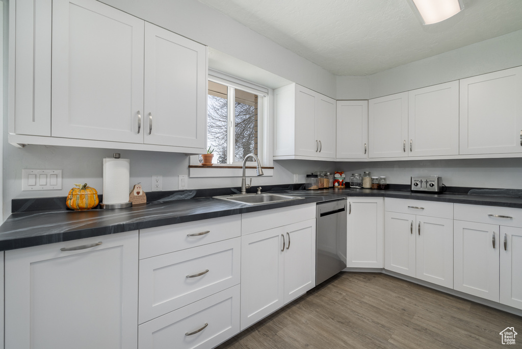 Kitchen featuring a sink, stainless steel dishwasher, dark countertops, and white cabinetry