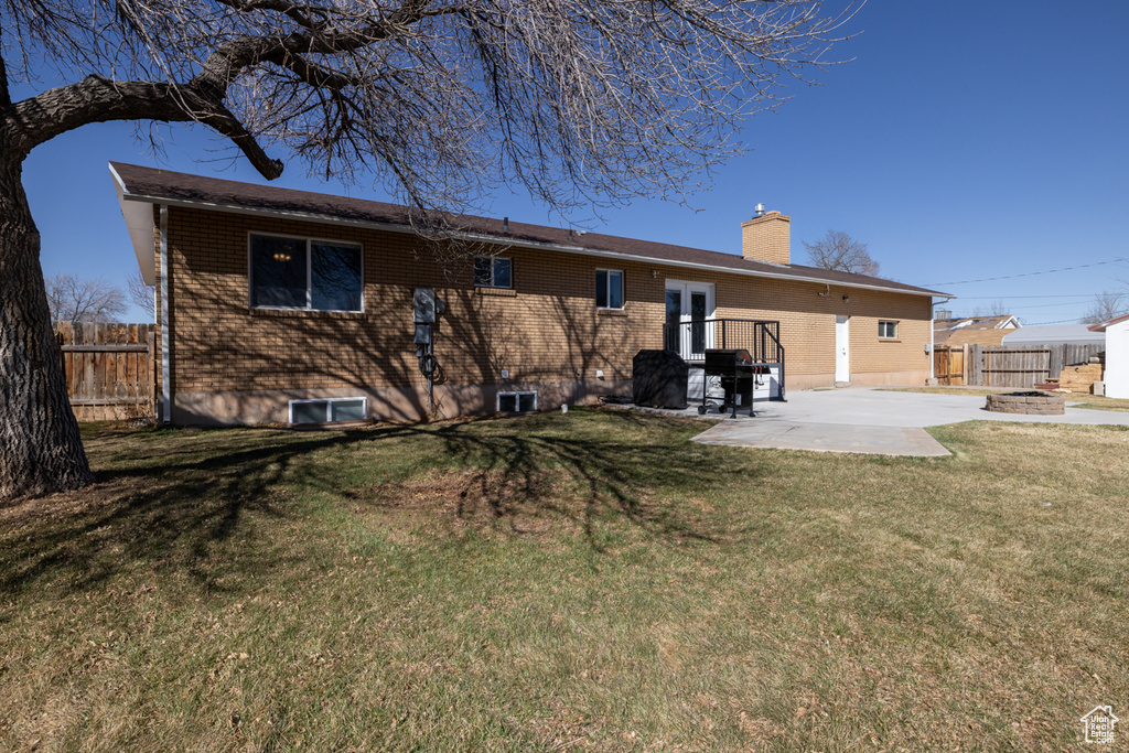 Rear view of house featuring brick siding, fence, a lawn, a chimney, and a patio