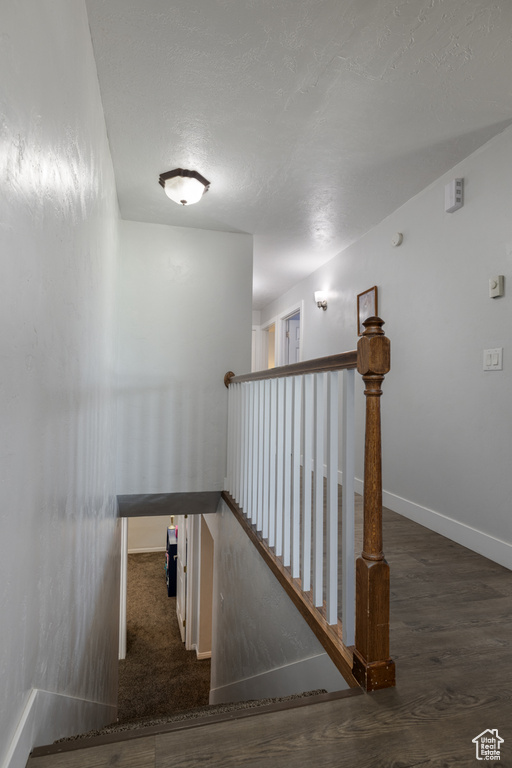 Stairs featuring a textured ceiling, baseboards, and wood finished floors