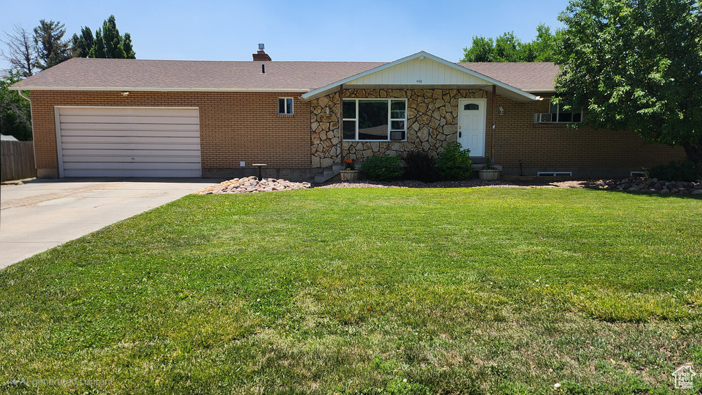 Ranch-style home with an attached garage, driveway, a front yard, a shingled roof, and stone siding