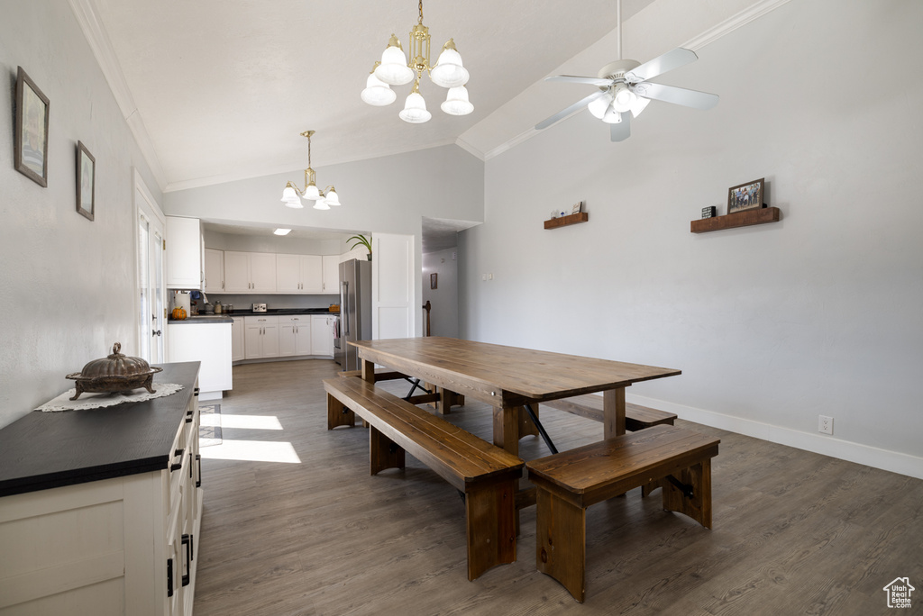 Dining area featuring baseboards, lofted ceiling, dark wood-style flooring, crown molding, and ceiling fan with notable chandelier