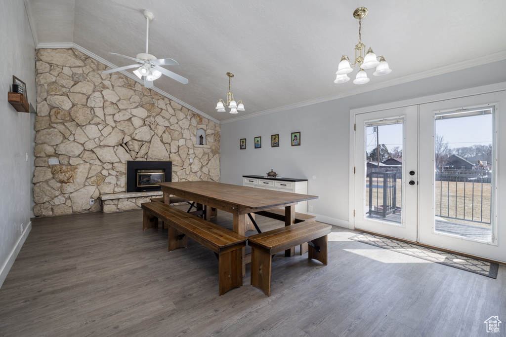 Dining space featuring wood finished floors, french doors, a stone fireplace, crown molding, and vaulted ceiling