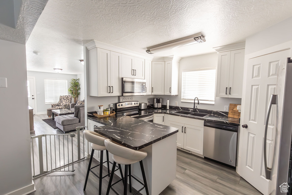 Kitchen featuring a sink, dark countertops, white cabinetry, stainless steel appliances, and a peninsula