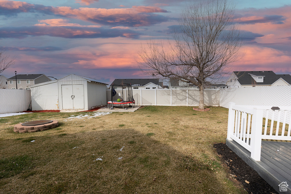 Yard at dusk with a fire pit, a trampoline, a fenced backyard, and a shed