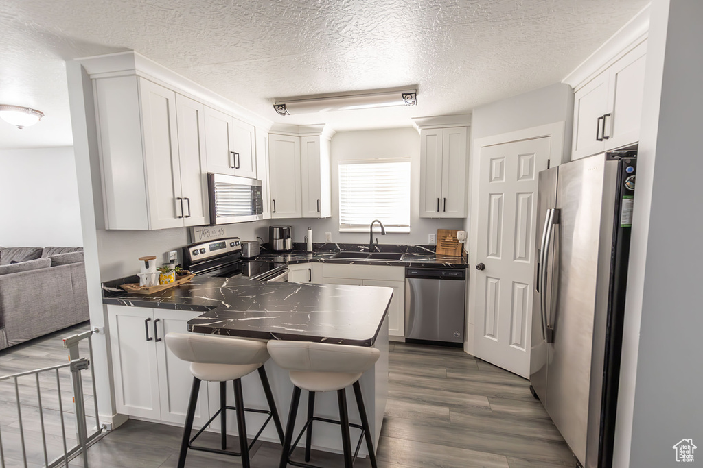 Kitchen with dark countertops, a kitchen breakfast bar, appliances with stainless steel finishes, a peninsula, and a sink