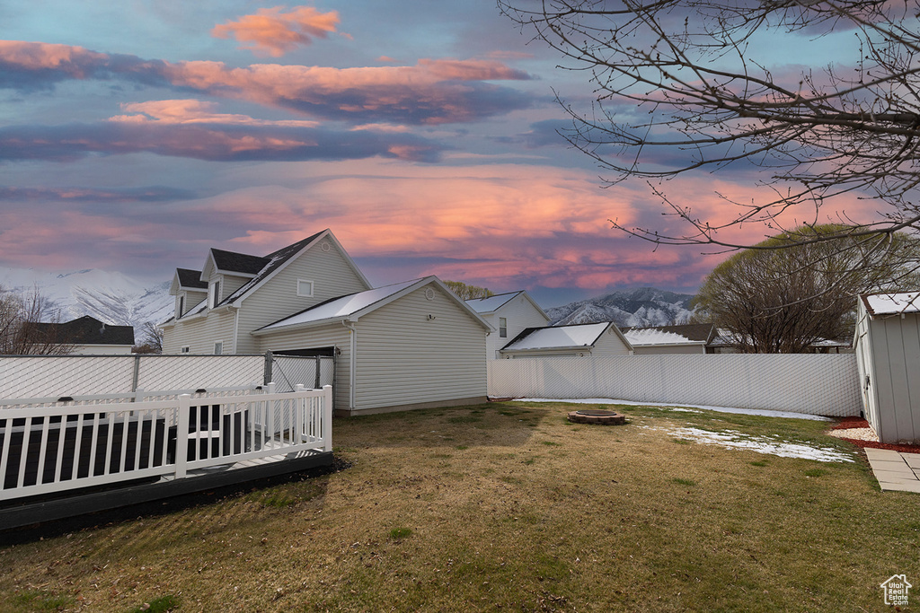 Yard at dusk featuring a deck with mountain view, an outdoor fire pit, and fence