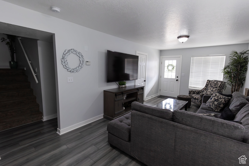 Living area with stairs, dark wood-type flooring, baseboards, and a textured ceiling
