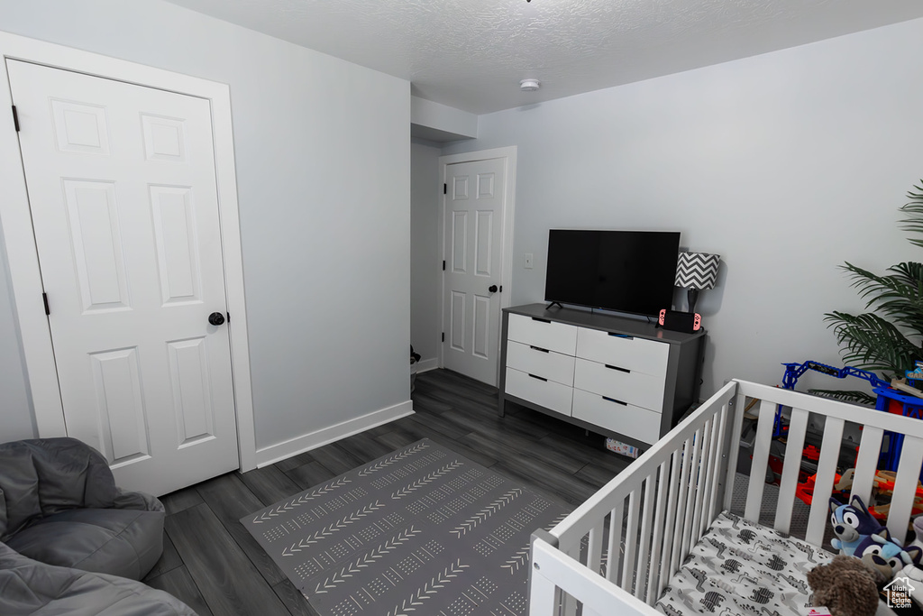 Bedroom featuring a nursery area, dark wood-style floors, baseboards, and a textured ceiling