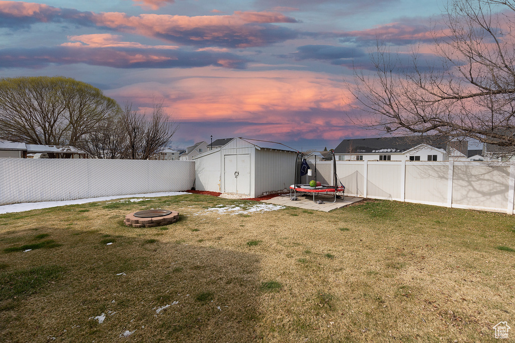 Yard at dusk featuring a storage shed, a fenced backyard, an outdoor structure, and an outdoor fire pit
