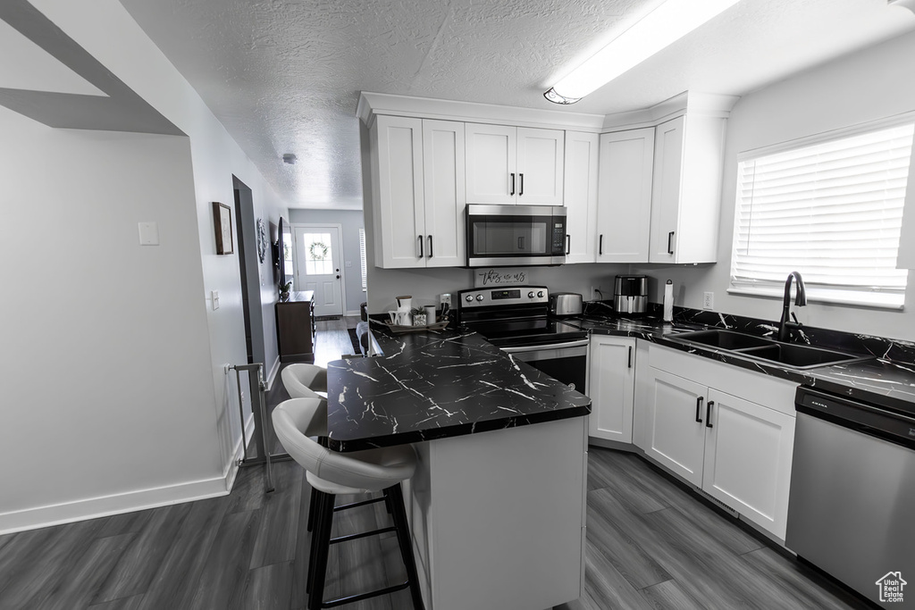 Kitchen featuring dark countertops, a center island, appliances with stainless steel finishes, white cabinetry, and a sink
