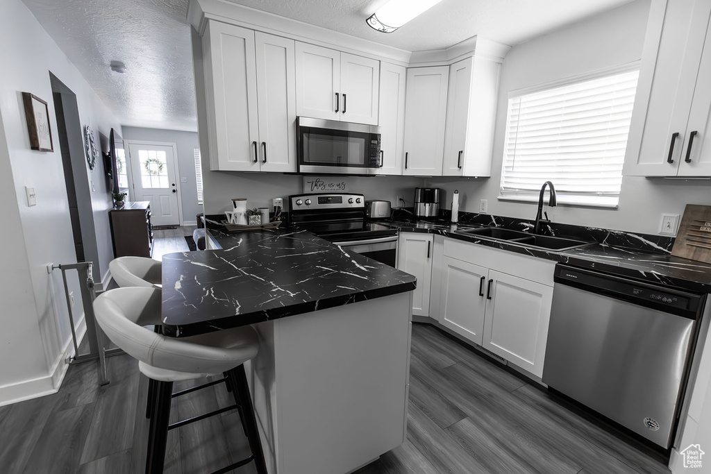 Kitchen featuring a sink, a kitchen breakfast bar, dark countertops, stainless steel appliances, and white cabinets