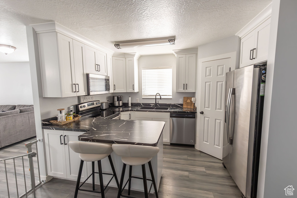 Kitchen with dark countertops, a sink, a peninsula, stainless steel appliances, and dark wood-style flooring