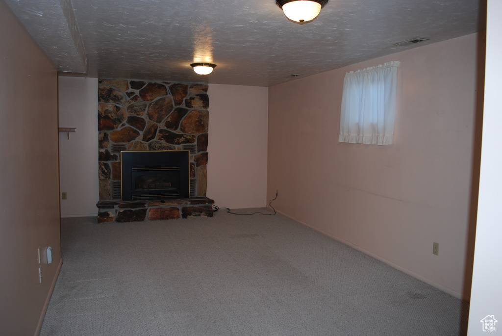 Unfurnished living room featuring a textured ceiling, carpet floors, and a stone fireplace