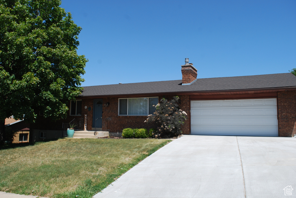 Ranch-style house featuring brick siding, a front lawn, an attached garage, concrete driveway, and a chimney