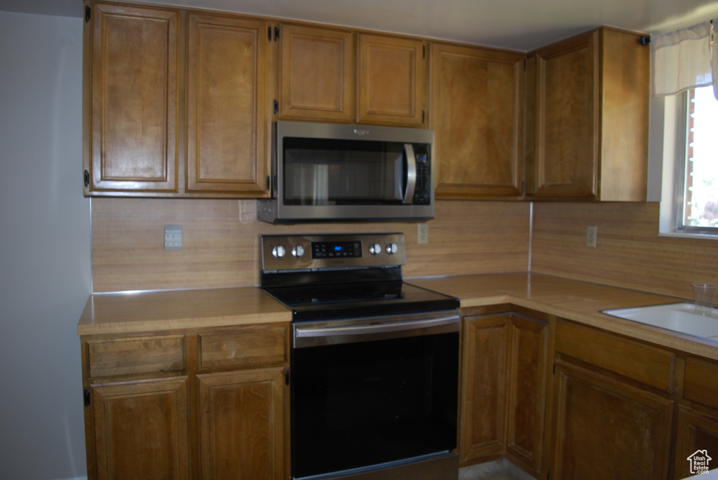 Kitchen featuring stainless steel appliances, light countertops, and brown cabinets