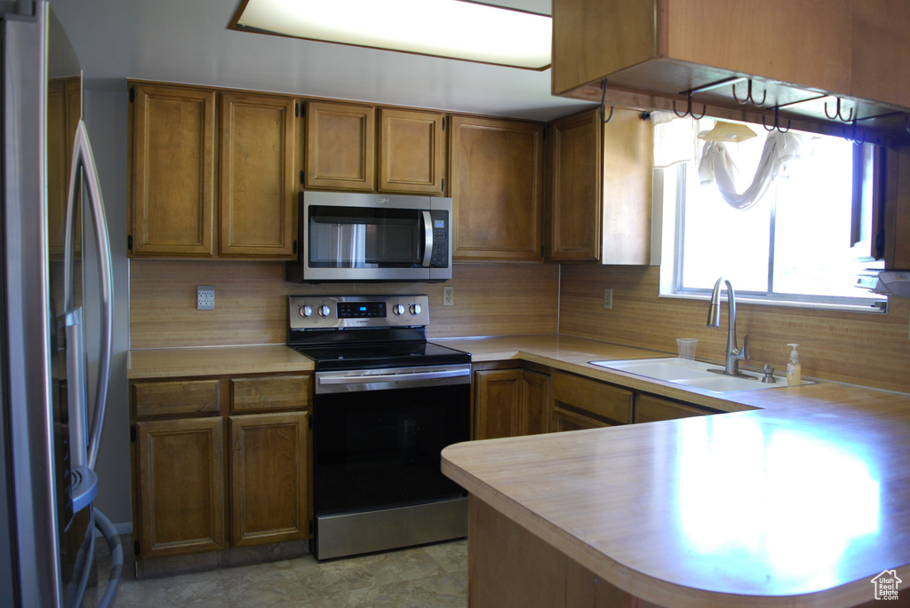 Kitchen with stainless steel appliances, light countertops, a peninsula, tasteful backsplash, and brown cabinets