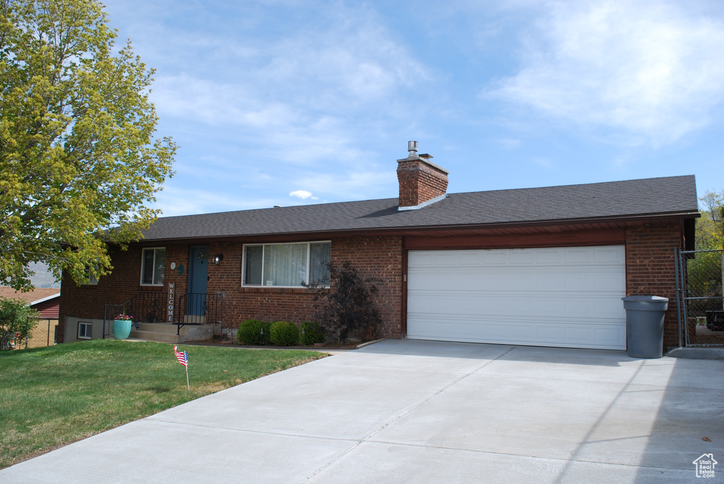 Ranch-style home featuring a chimney, brick siding, a garage, driveway, and a front yard