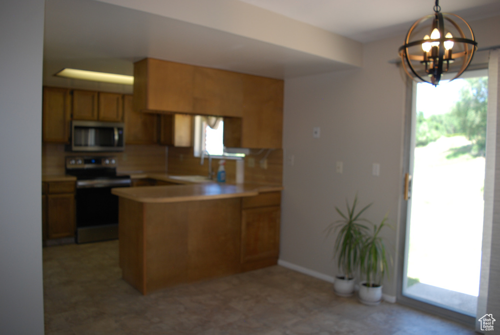 Kitchen featuring stainless steel appliances, a peninsula, a chandelier, brown cabinetry, and light countertops