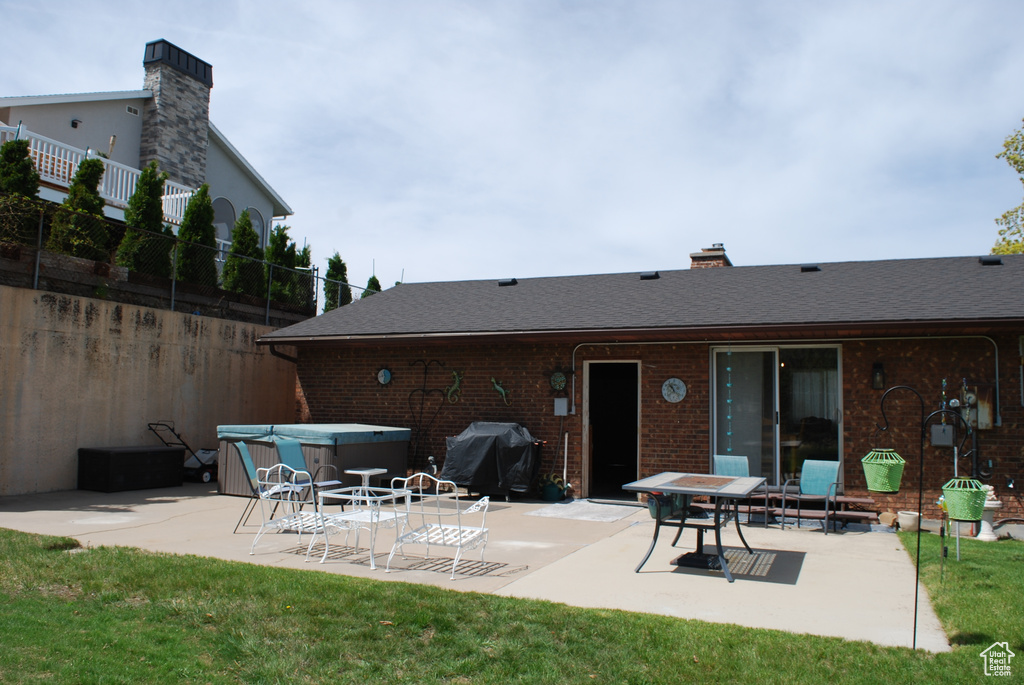 Rear view of house with brick siding, a shingled roof, a patio area, and a hot tub