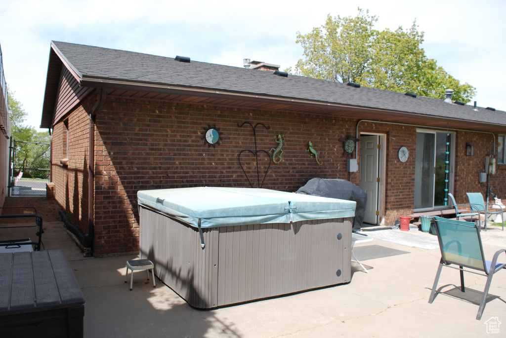 Rear view of property with brick siding, a patio, and a hot tub
