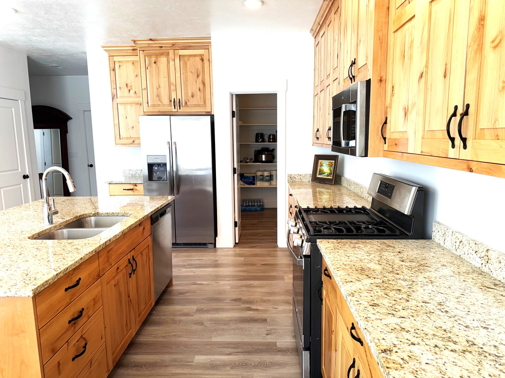 Kitchen featuring light stone counters, a center island with sink, light wood finished floors, a sink, and appliances with stainless steel finishes