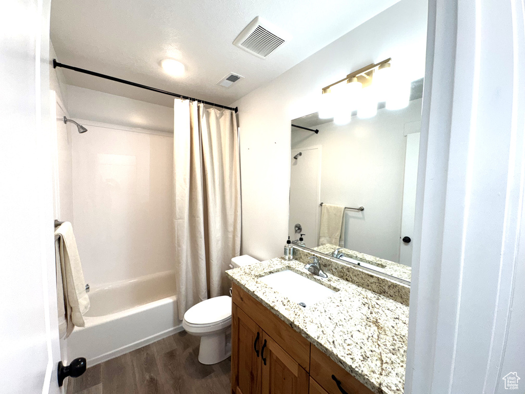 Full bathroom with visible vents, toilet, shower / tub combo, and wood finished floors