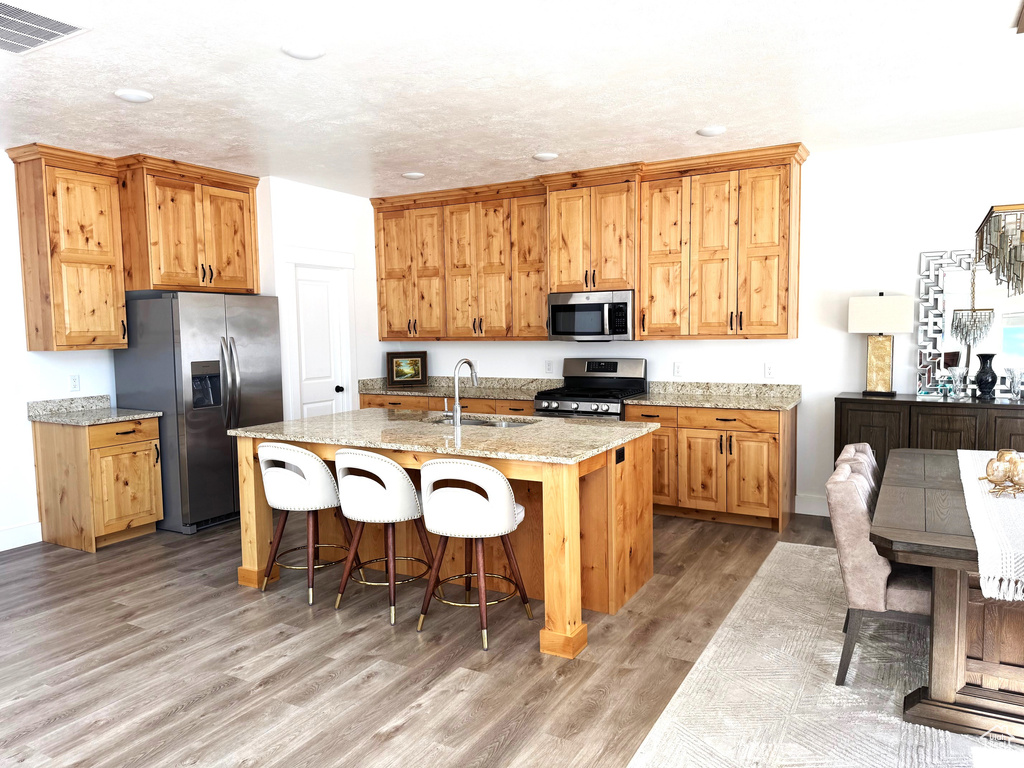 Kitchen with visible vents, a breakfast bar, a sink, stainless steel appliances, and light wood finished floors