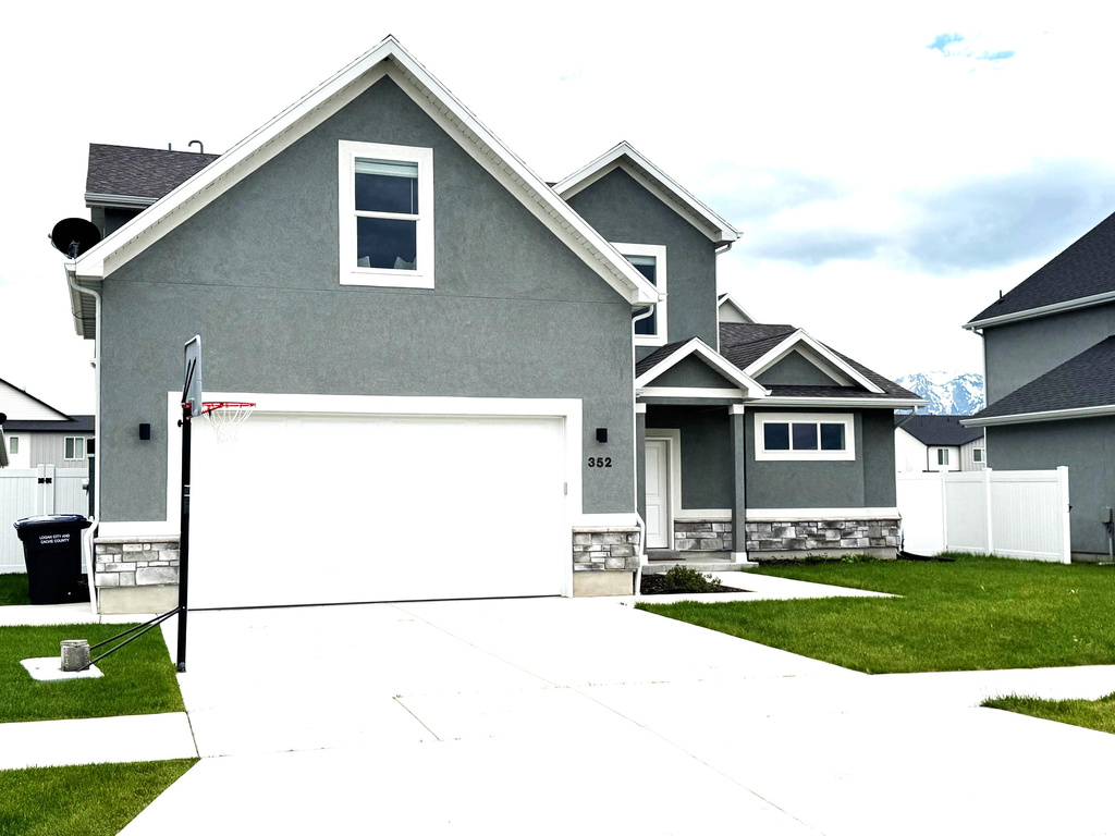 View of front of property featuring stone siding, driveway, stucco siding, and a garage
