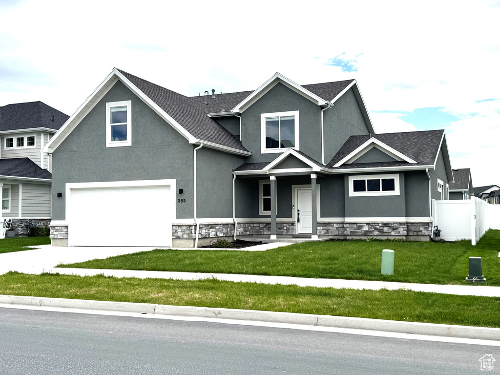 View of front of home with a garage, stucco siding, stone siding, driveway, and covered porch