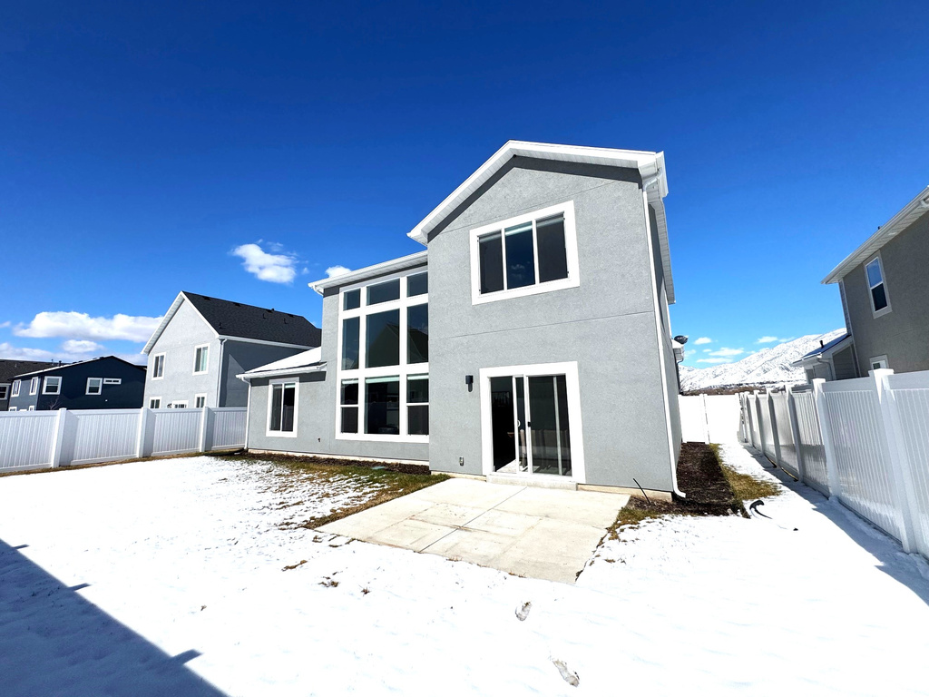 Snow covered back of property with stucco siding, a fenced backyard, and a patio area