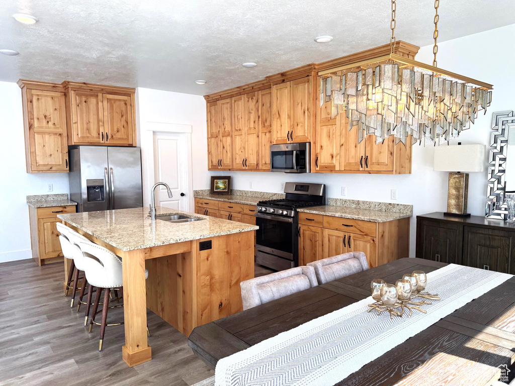 Kitchen with a sink, a breakfast bar area, wood finished floors, stainless steel appliances, and a kitchen island with sink