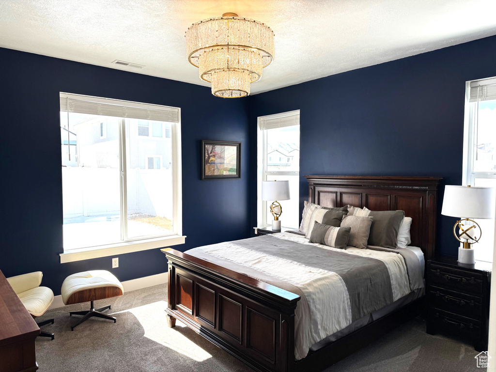 Carpeted bedroom featuring a notable chandelier, visible vents, a textured ceiling, and baseboards
