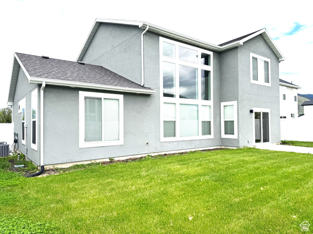Back of property with stucco siding, a lawn, and central AC unit