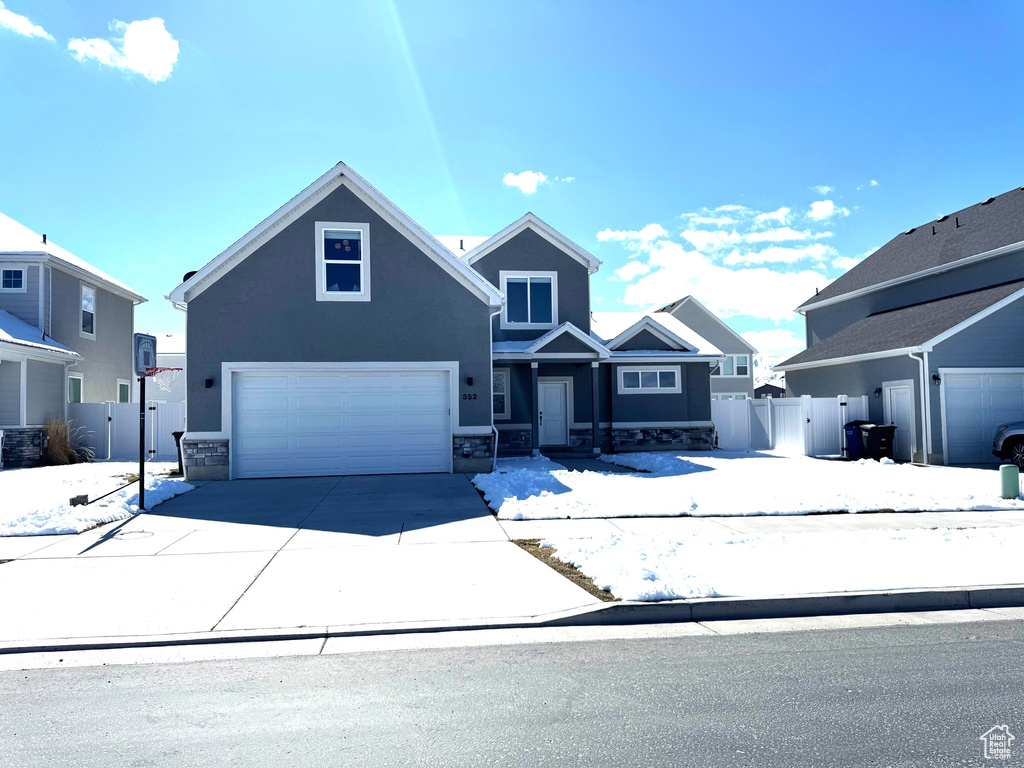 View of front of property featuring fence, driveway, stucco siding, stone siding, and a garage