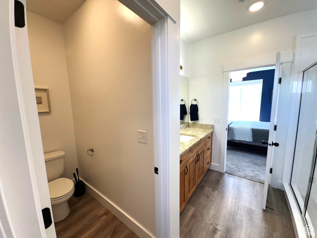 Bathroom with toilet, wood finished floors, connected bathroom, baseboards, and vanity