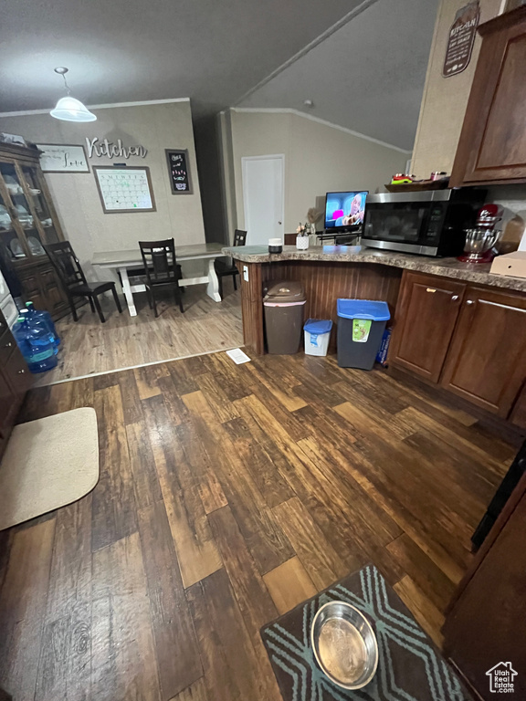 Kitchen with lofted ceiling, a peninsula, ornamental molding, wood-type flooring, and stainless steel microwave