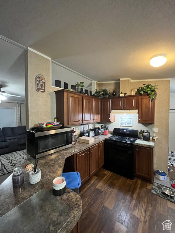 Kitchen with black gas stove, dark wood-style flooring, ceiling fan, under cabinet range hood, and stainless steel microwave