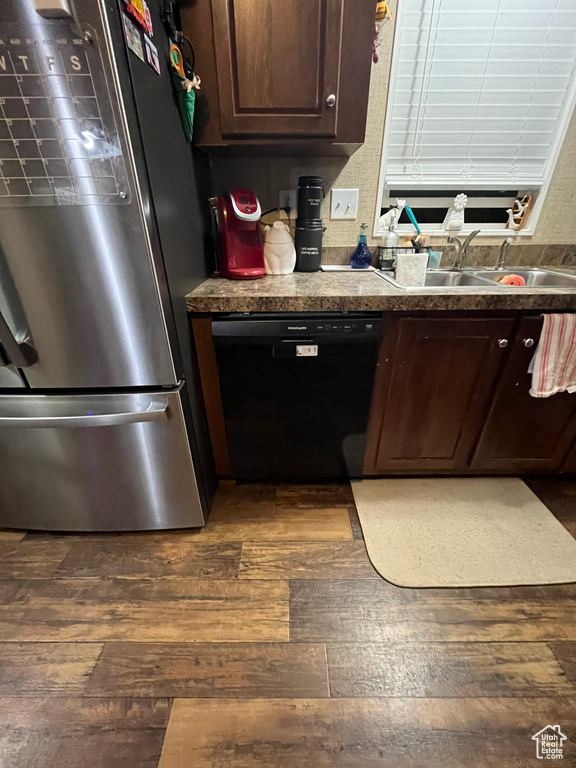 Kitchen featuring a sink, black dishwasher, dark wood finished floors, and freestanding refrigerator