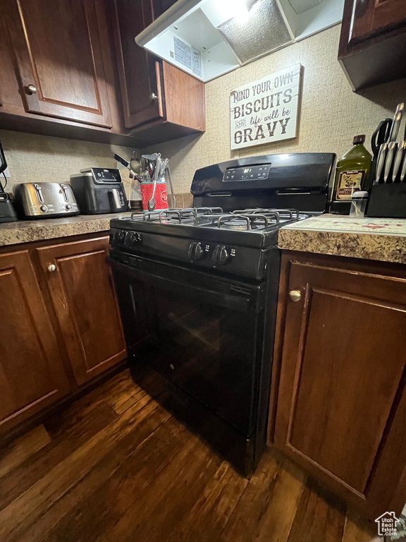Kitchen with black range with gas cooktop, light countertops, wall chimney exhaust hood, and dark wood-style flooring