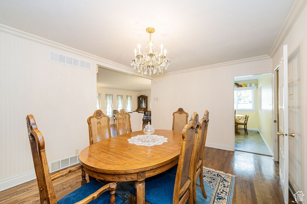 Dining space featuring crown molding, plenty of natural light, wood finished floors, a chandelier, and baseboards