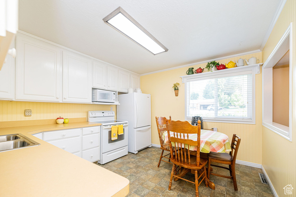 Kitchen with white appliances, stone finish floors, white cabinets, light countertops, and ornamental molding