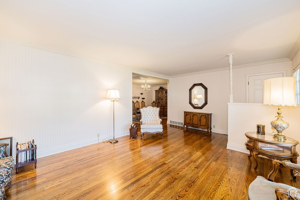 Living area with wood finished floors, a chandelier, ornamental molding, and baseboards