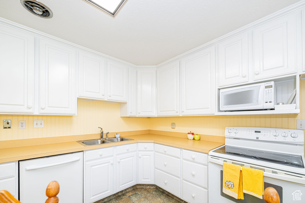 Kitchen featuring white appliances, a sink, white cabinetry, and light countertops