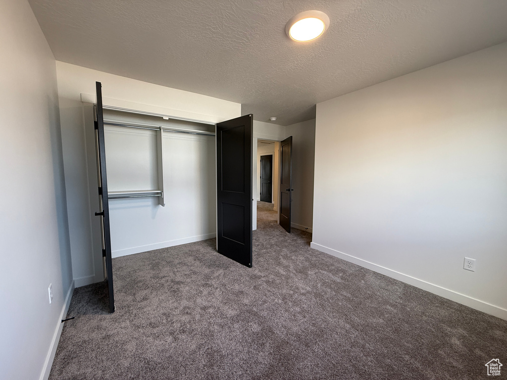 Unfurnished bedroom with a closet, dark carpet, a textured ceiling, and baseboards