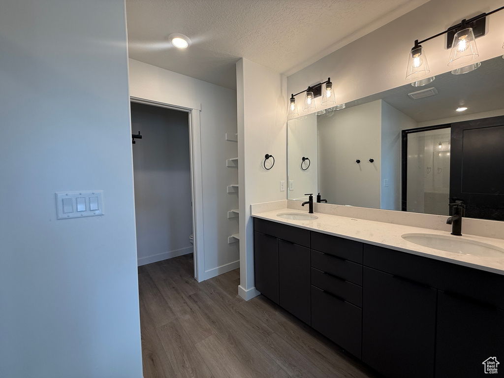 Bathroom featuring double vanity, a textured ceiling, wood finished floors, and a sink